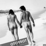 Nude couple walking on the beach holding hands.